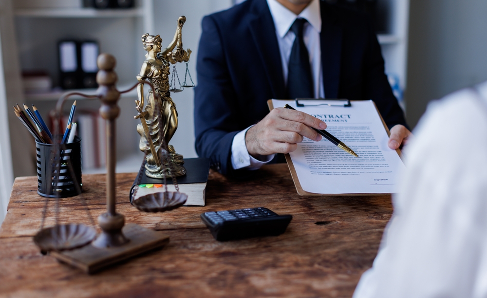 Lawyer presenting a contract to a client at a desk with a scales of justice statue