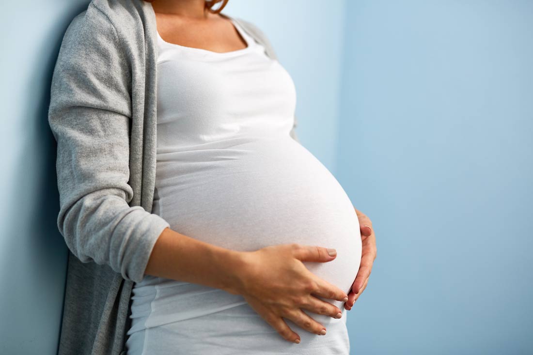 mid-section portrait of woman during last months of pregnancy holding her belly leaning against wall
