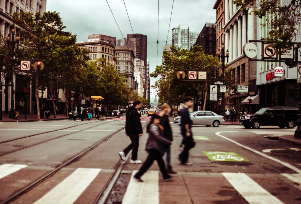 pedestrians crossing the street with motor vehicles driving behind them