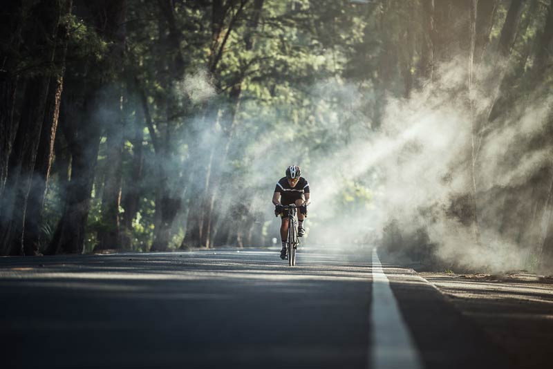 man bicycling on tree-lined asphalt road