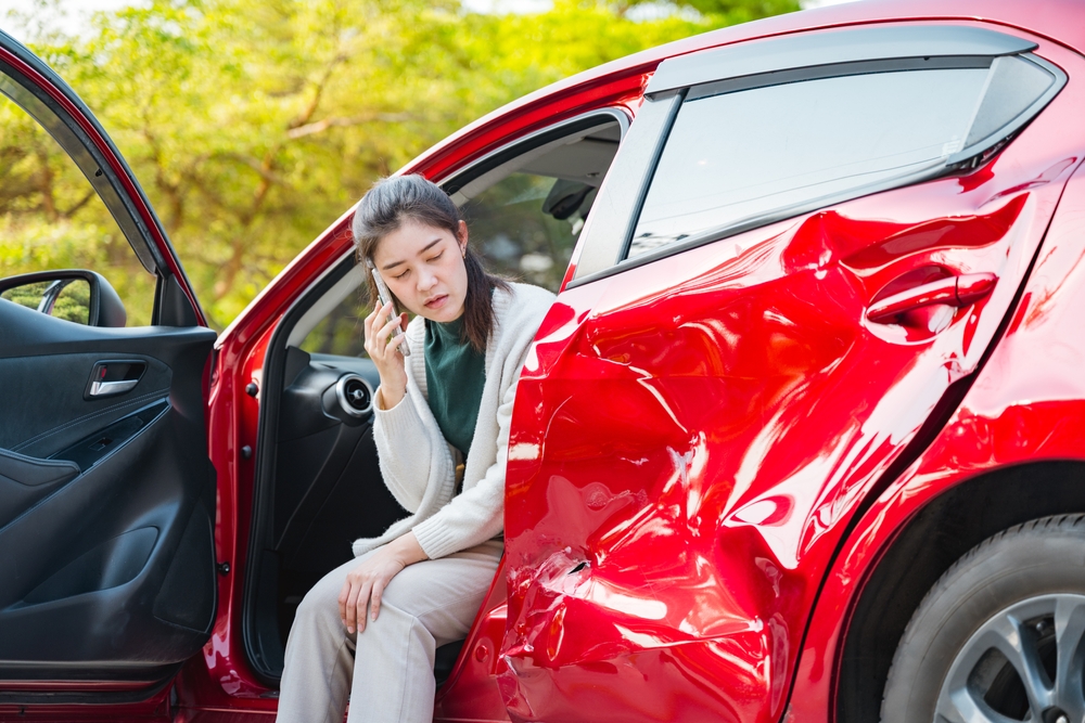 Woman sitting in a red car with a dented door after a collision