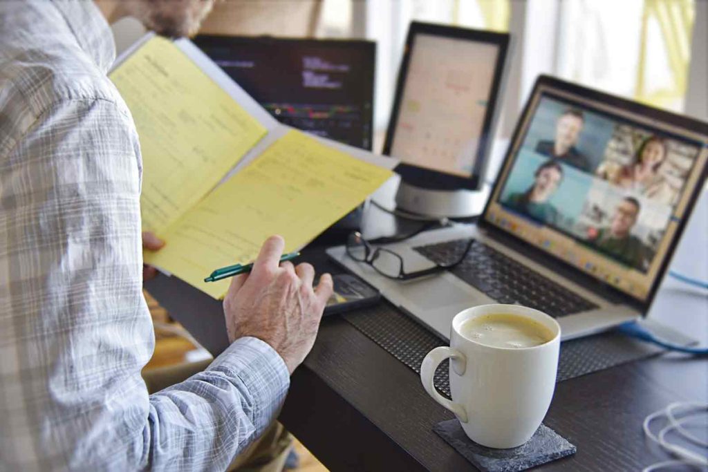 Man at home office signing documents with virtual chat on computer screen with people in virtual deposition