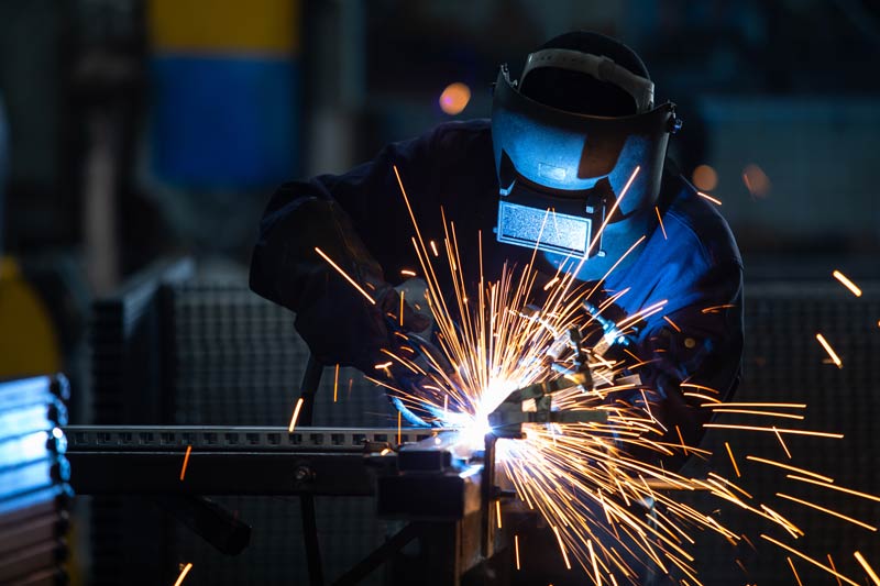 workers wearing industrial uniforms and welded iron mask at steel welding plant